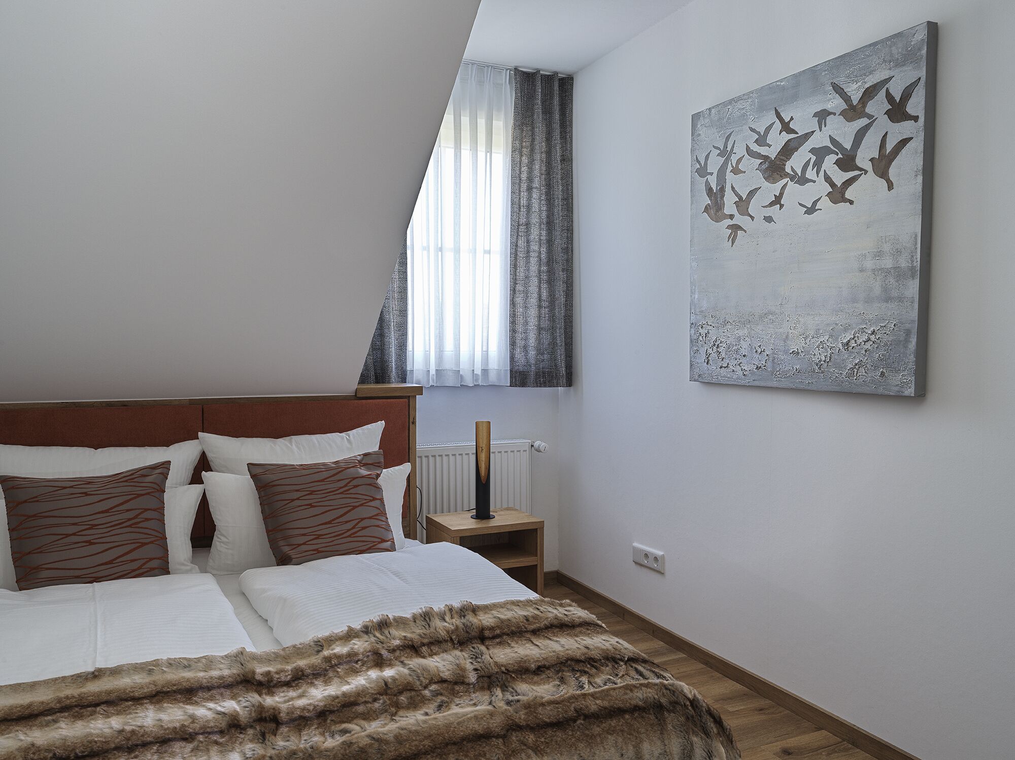 A bedroom with a bed, a nightstand, a radiator, and a painting of birds on the wall.