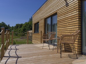 Une cabane en bois dotée d’une terrasse, de deux fauteuils en osier et d’une barrière en corde.