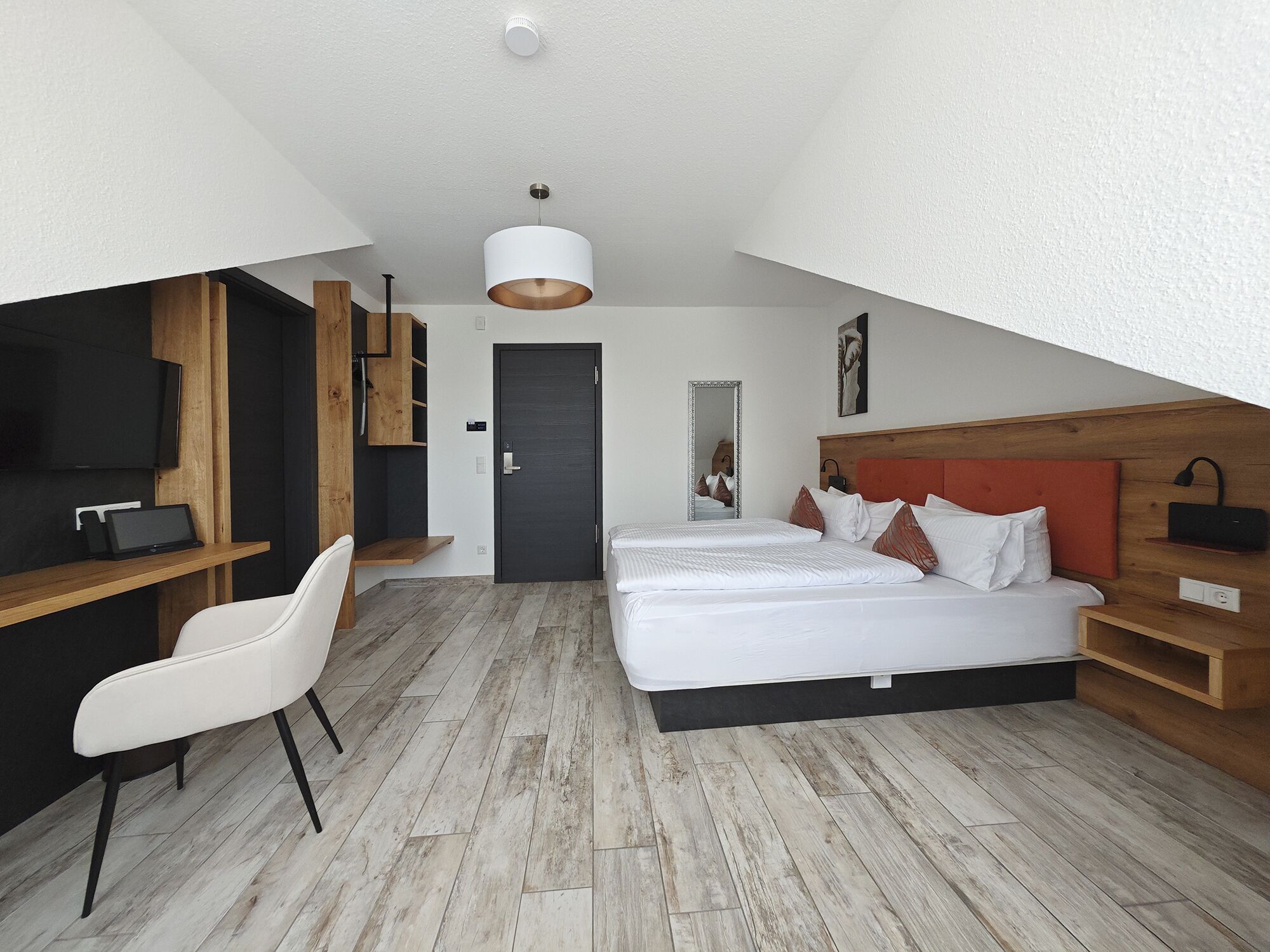 Ein modernes Schlafzimmer mit Bett, Schreibtisch, Stuhl und einem großen Spiegel.