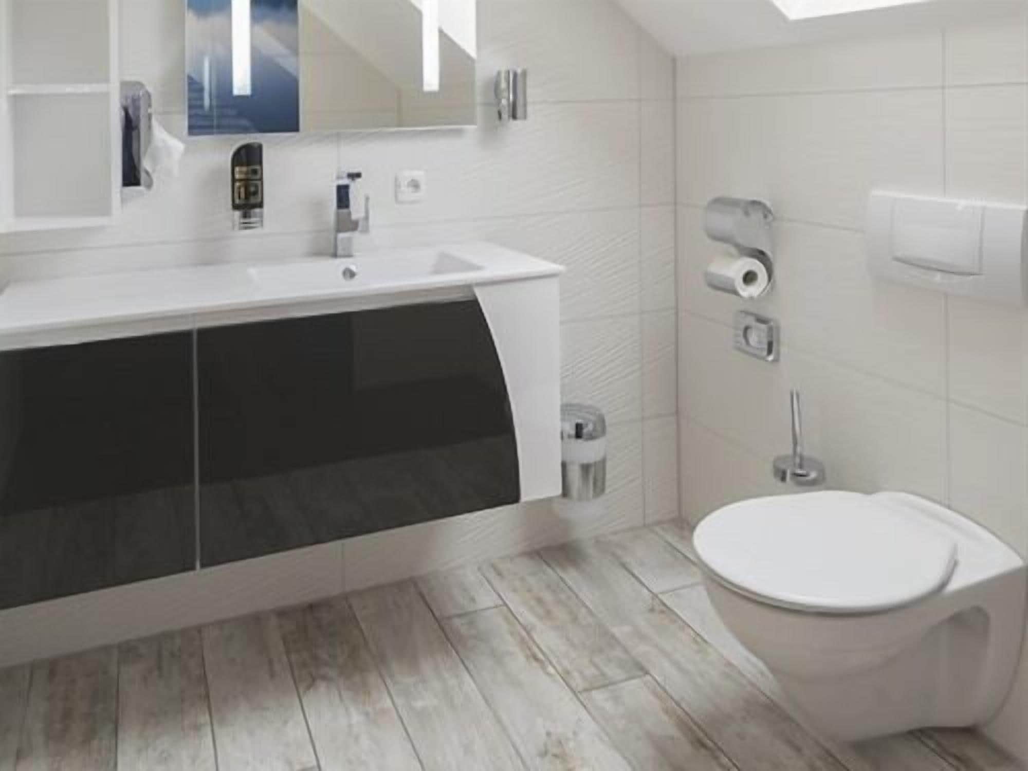Et moderne badeværelse med hvid vask, spejl og toilet.