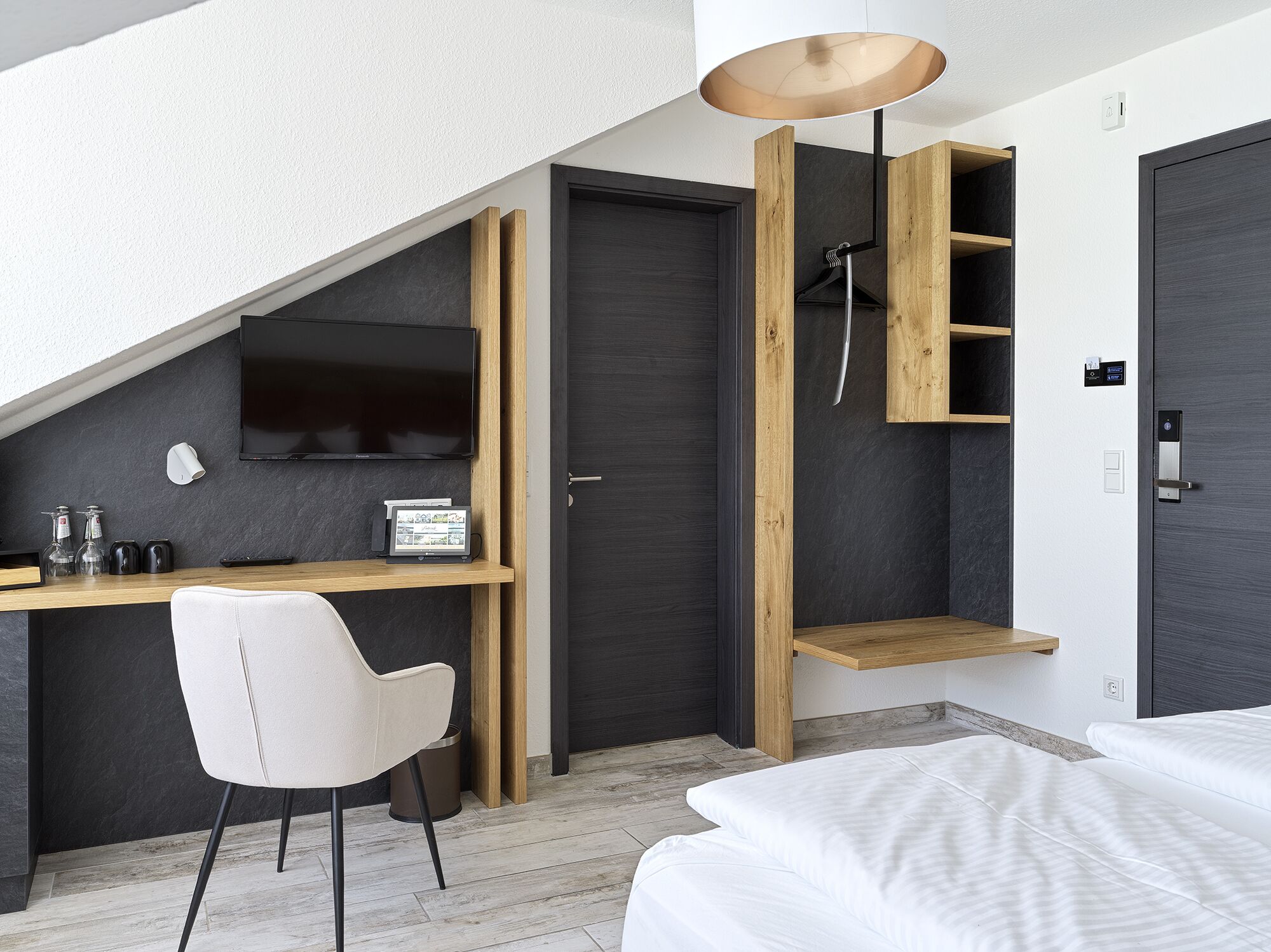 A modern bedroom with a sloped ceiling, a desk with a chair, a bed, and a built-in wardrobe.