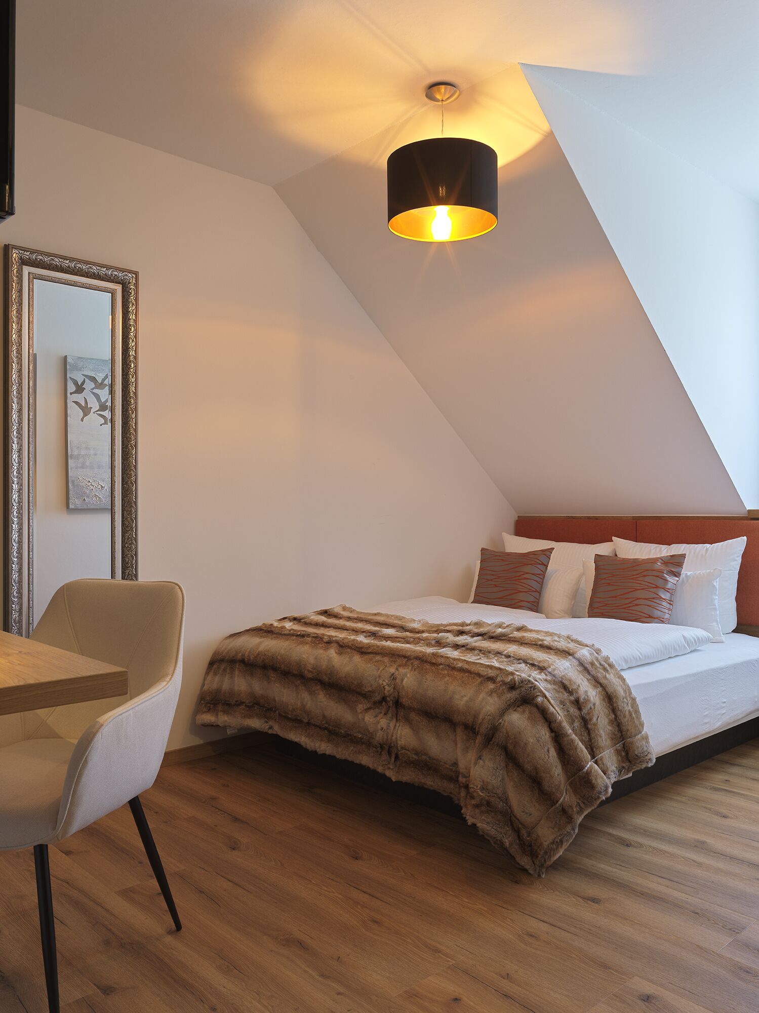 A bedroom with a bed, a chair, a mirror, and a ceiling light fixture.