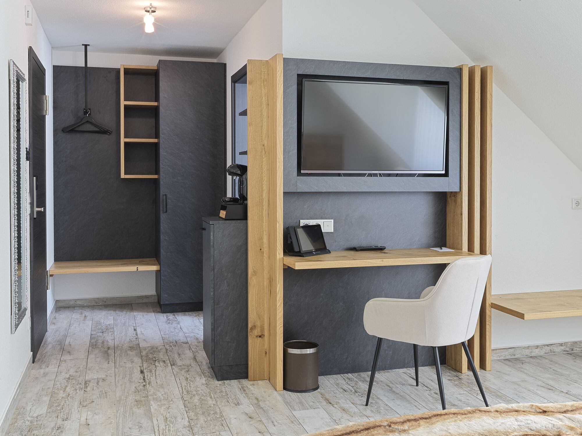 A modern, compact bedroom with a built-in desk, a television, and a hanging light fixture.