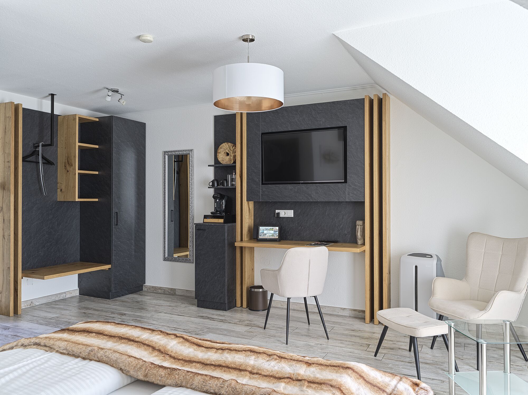 Un dormitorio moderno con techo estilo loft, una cama grande con una manta de piel, un escritorio con una computadora, un televisor y una silla.