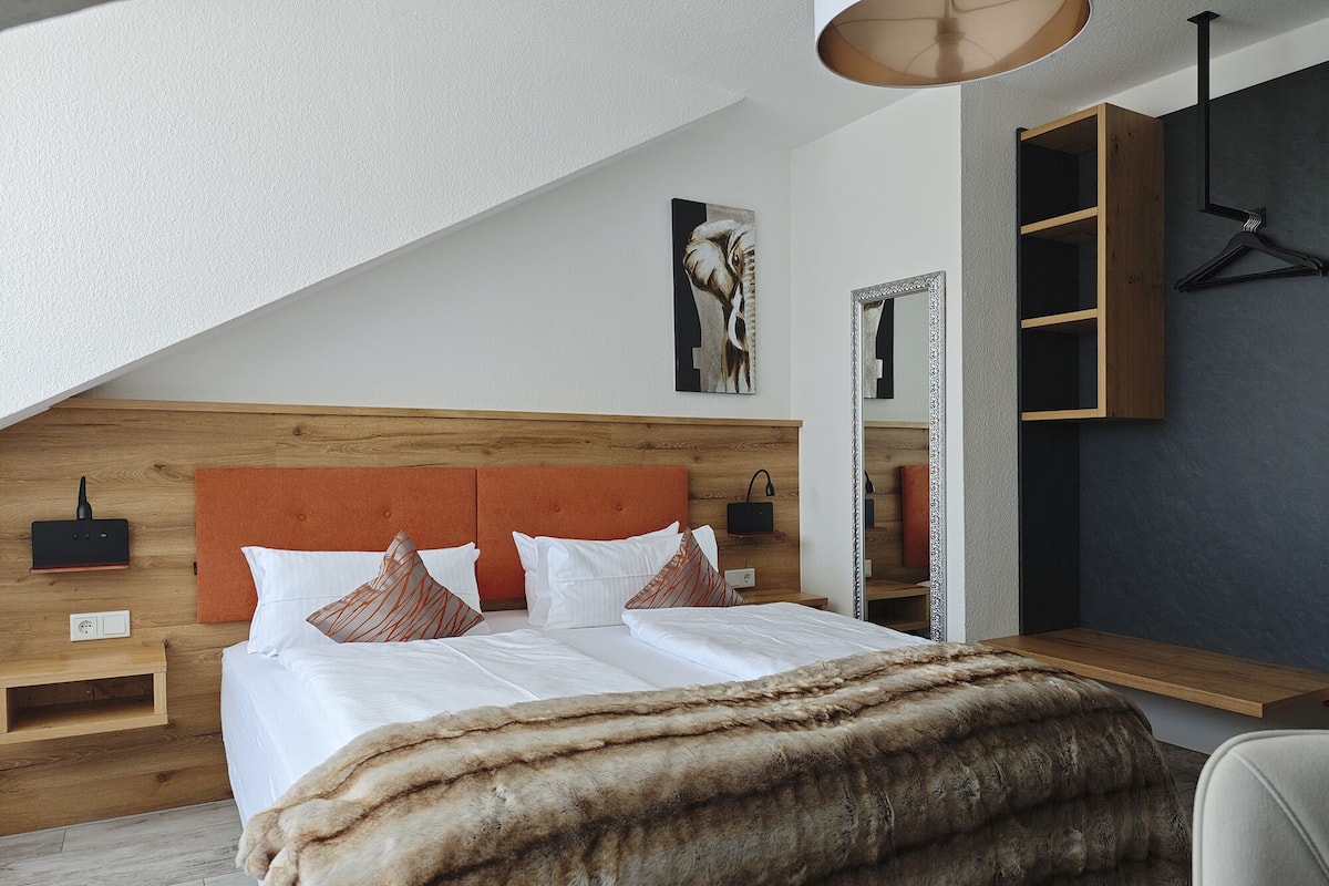 Une chambre à coucher moderne avec une tête de lit en bois, un grand lit avec une literie blanche, un plaid en fausse fourrure, une table de chevet avec une lampe et un luminaire suspendu.