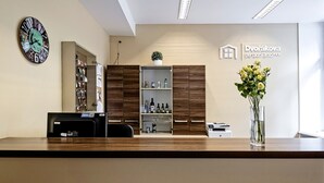 A reception area with a wooden reception desk, a clock, a shelf with various items, and a sign for Dvořákova pension Bmo. - Penzion Dvorákova (Brno)
