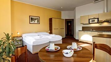 Una camera d'albergo con un letto, un tavolo da pranzo con tazze e piattini, una pianta e angolo cottura.