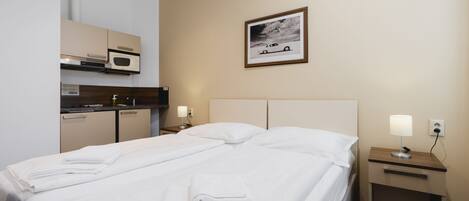 A hotel room with a bed, two bedside tables, a nightstand, a microwave, a small cabinet, and a framed picture on the wall.
