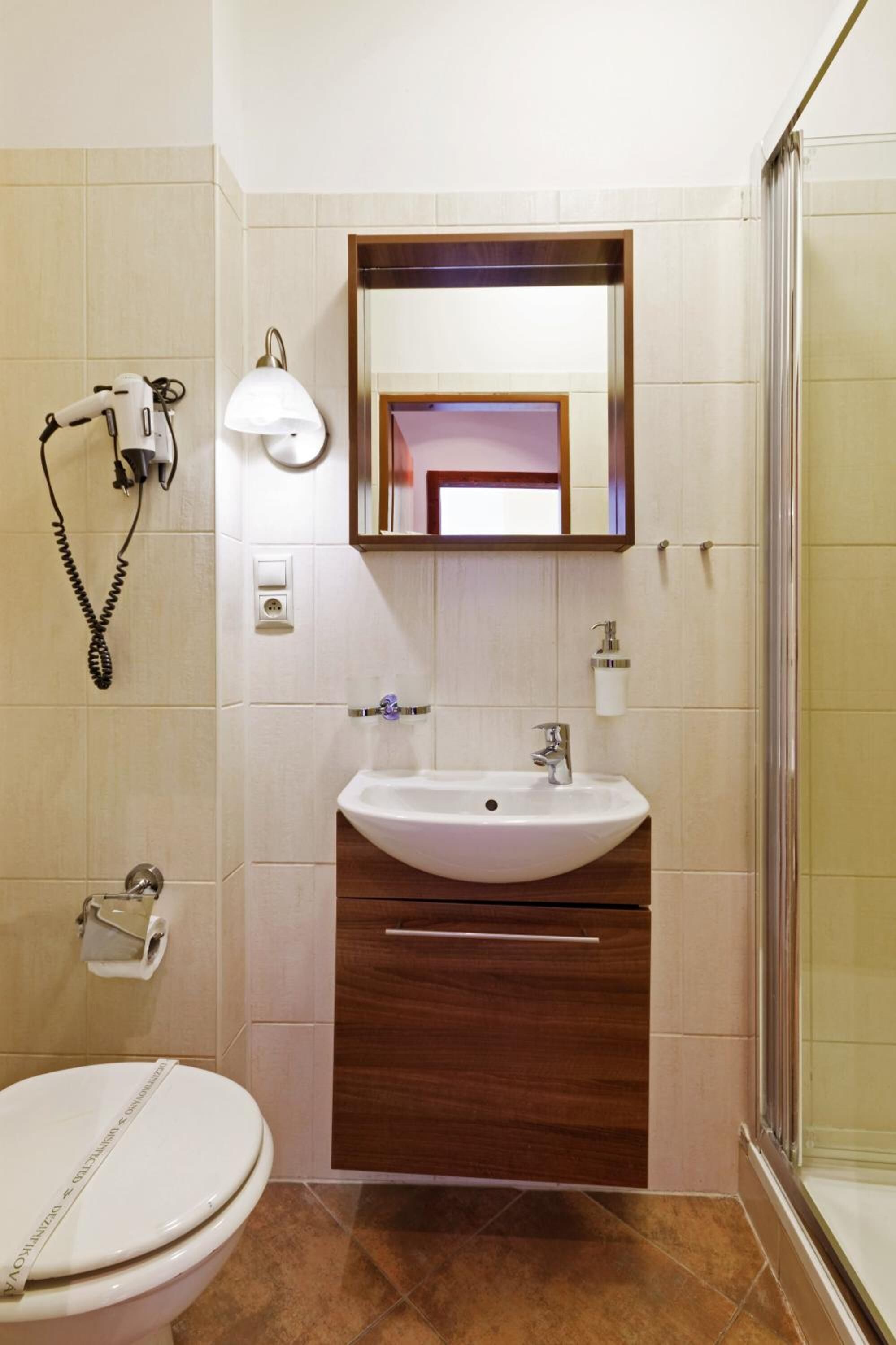 A bathroom with a white sink, a mirror above it, a towel dispenser, and a toilet.