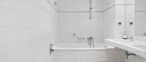 A modern bathroom with white tiles, a bathtub, a shower, and a sink with a mirror.