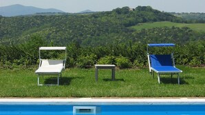 A swimming pool with two lounge chairs and a small table, surrounded by lush greenery and hills in the background. - Fattoria Nuova Pievanella (Civitella Paganico)