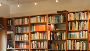 A library with wooden bookshelves filled with books, a table with chairs, and a tiled floor. - Fattoria Nuova Pievanella (Civitella Paganico)