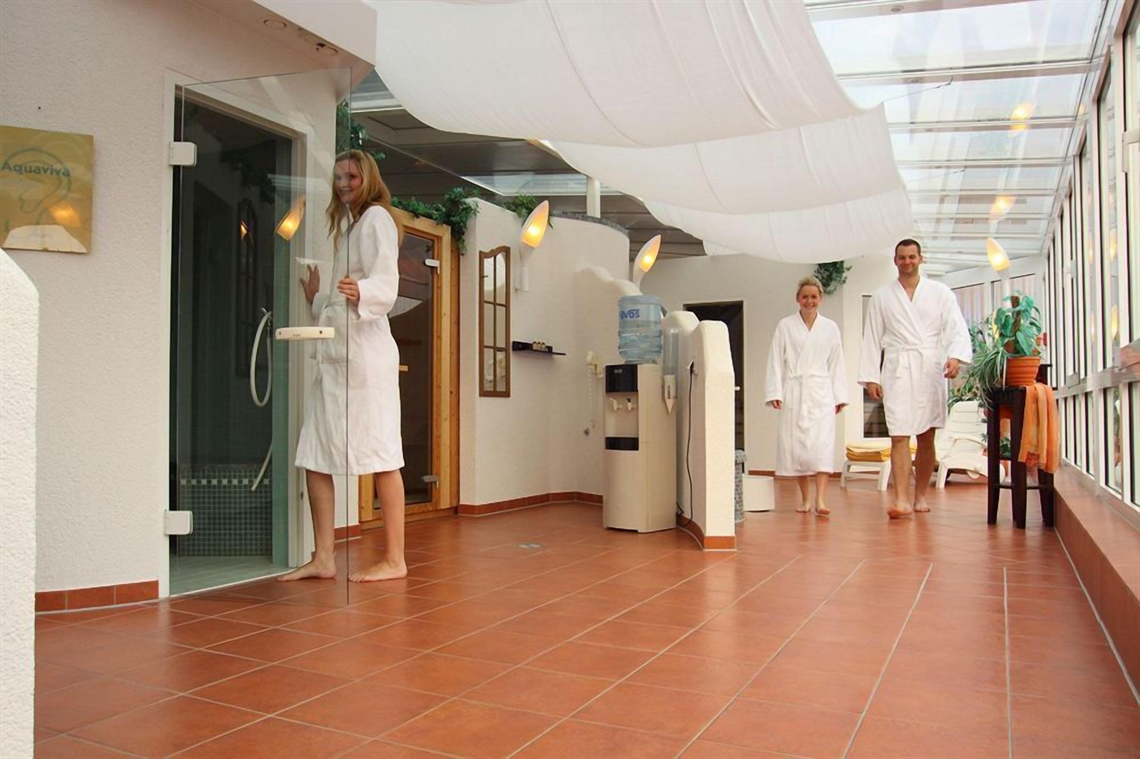 Ein Wellnessbereich mit Glastür, Wasserspender und einer Sitzecke mit Pflanze.