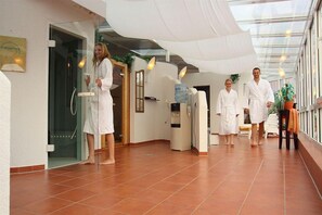 A spa area with a glass door entrance, a water dispenser, and a seating area with a plant. - Hotel Novum (Hinte)