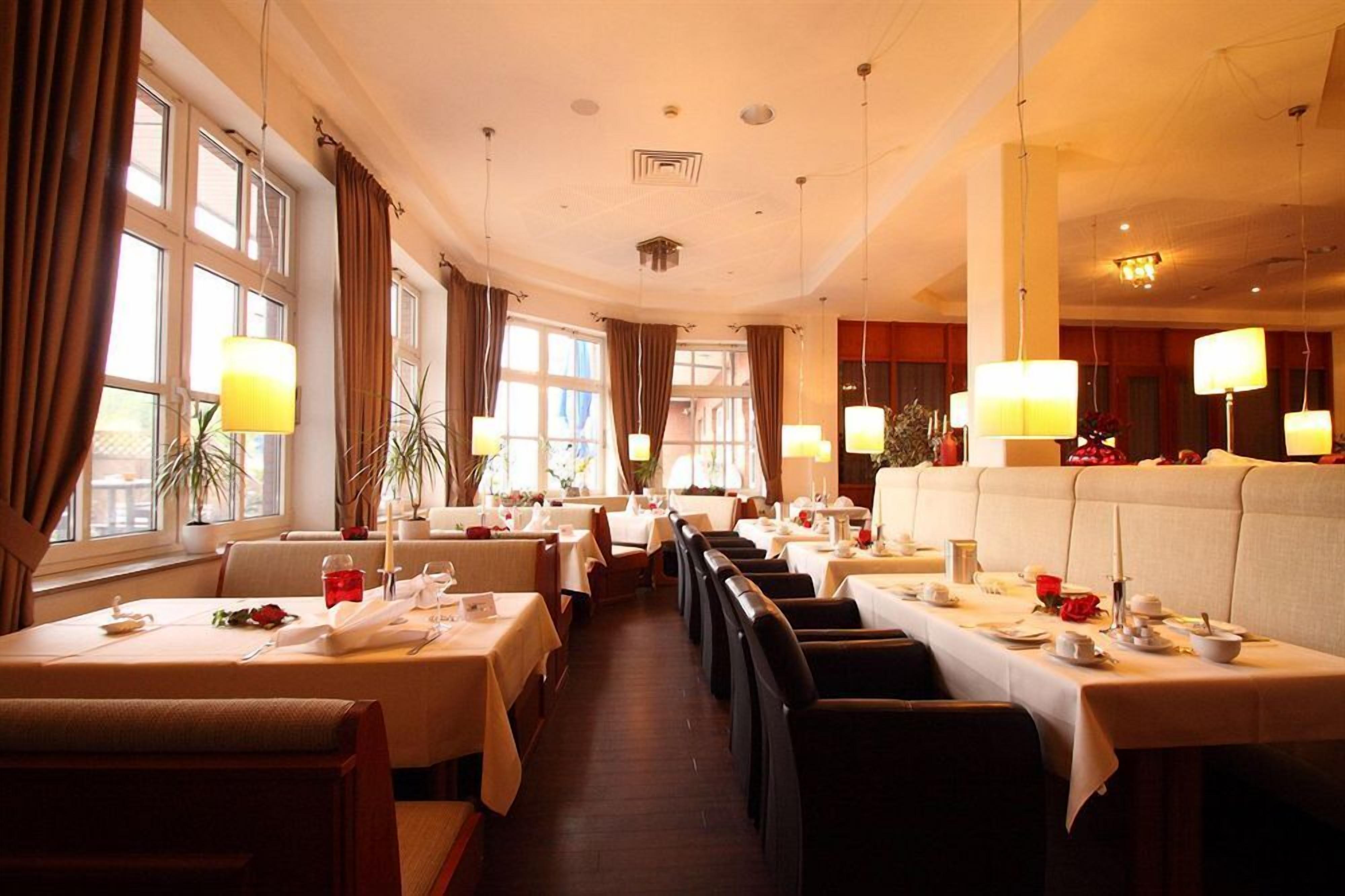 Ein Restaurant mit mehreren Tischen und Sitzecken, großen Fenstern und hängenden Lampen.