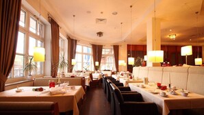 En restaurang med många bord och avskilda sittplatser, stora fönster och hängande lampor.