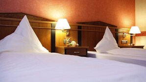 Ett hotellrum med två sängar, sänggavlar i trä, sängbord med lampor och ett litet sidobord med en klocka och dekorativa föremål.