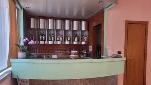 A bar area with a counter, shelves of bottles, glasses, and a chair. - Hotel Lux (Alessandria)