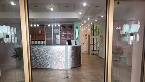 A reception area with a marble counter, a plant, and a staircase leading to an upper floor. - Hotel Lux (Alessandria)