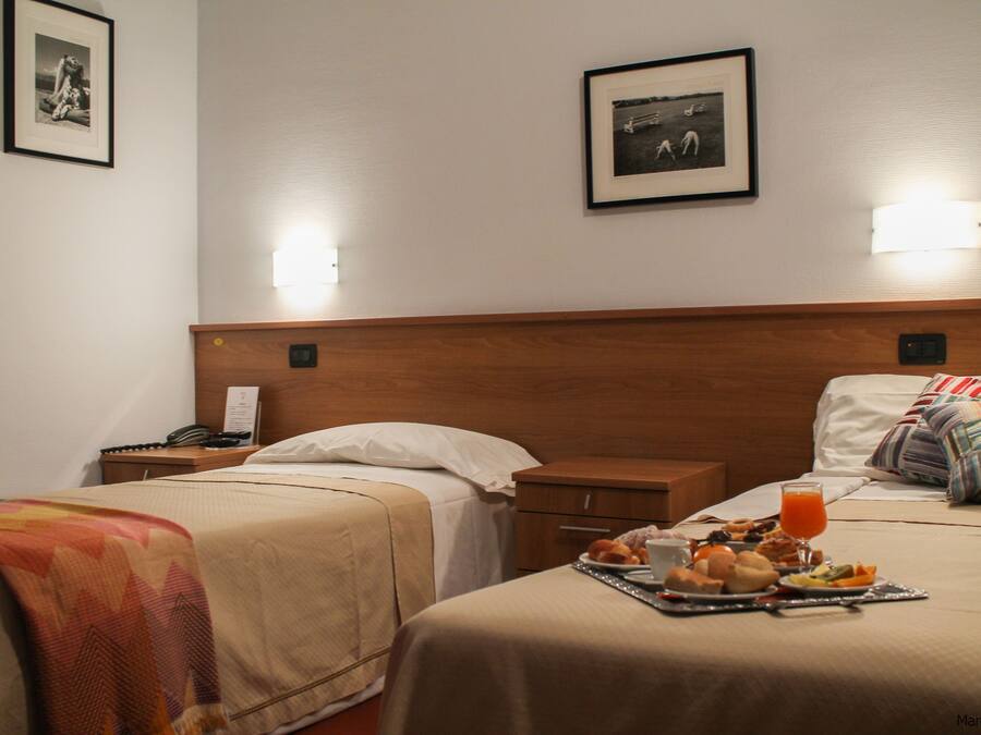 Et hotelværelse med to senge, et natbord med telefon og en bakke med morgenmadsprodukter, heriblandt appelsinjuice.