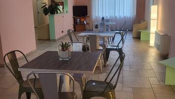Ein Essbereich mit einem langen Tisch, Stühlen, einem Fernseher und einer Pflanze.