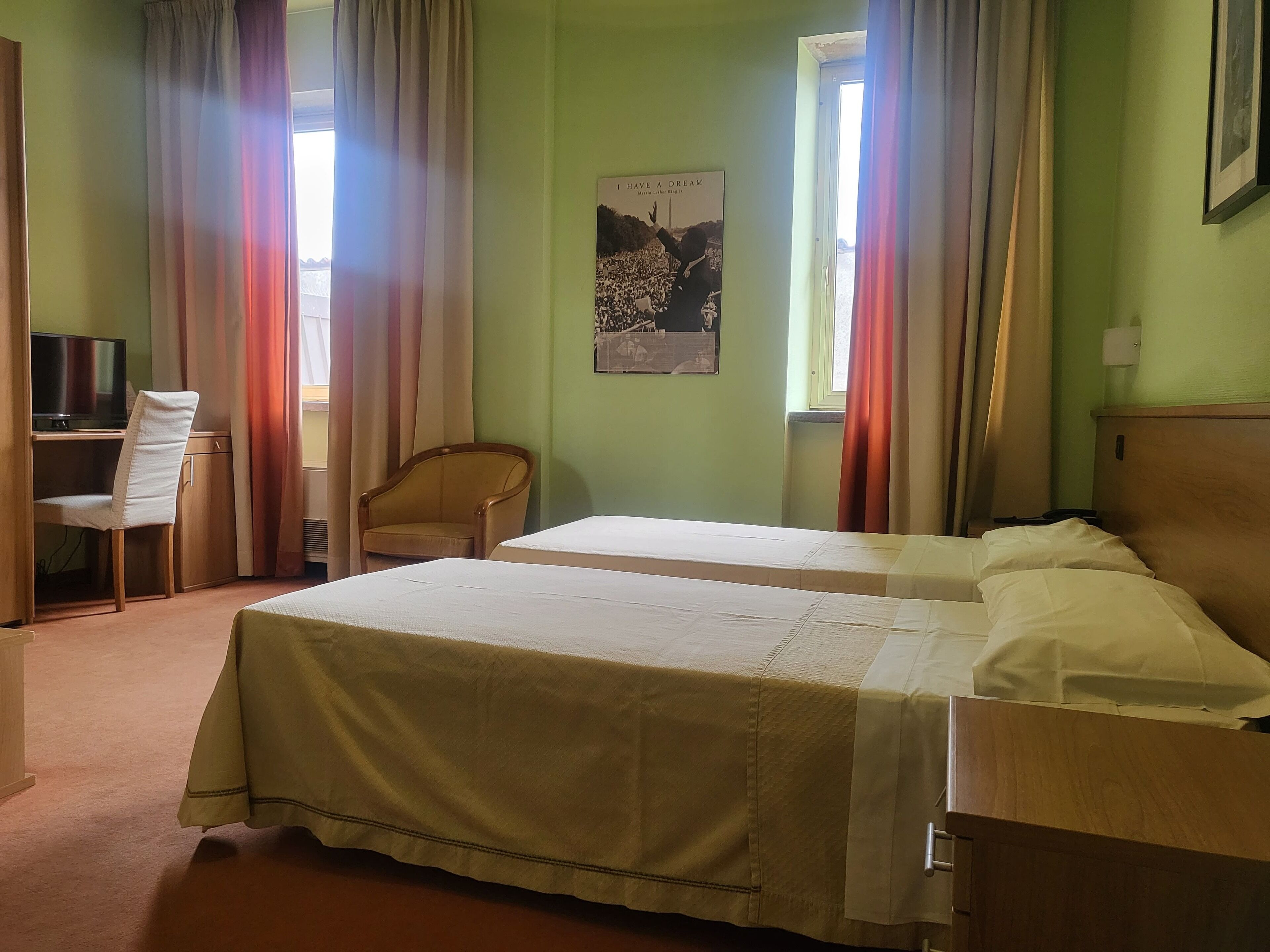 A hotel room with two beds, a desk with a chair, a television, and a poster on the wall.
