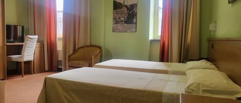 A hotel room with two beds, a desk with a chair, a television, and a poster on the wall.