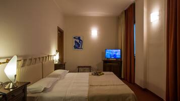 Una camera d'albergo con un letto, una televisione, una scrivania con una lampada e una luce a parete.
