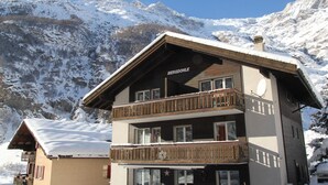 A multi-story building with balconies, a sign reading "BERGDÖHL," and a snowy mountain backdrop. - Haus Bergdohle (Randa)