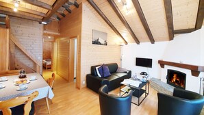 A cozy cabin interior with a dining area, a sofa, a fireplace, and a staircase leading to another room. - Haus Bergdohle (Randa)