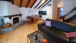 A cozy living room with a fireplace, a dining area, and a kitchen. - Haus Bergdohle (Randa)