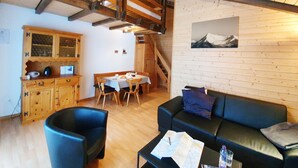 A cozy room with a wooden ceiling, a dining table with chairs, a sofa, and a black trash bin. - Haus Bergdohle (Randa)