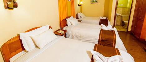 A hotel room with three beds, each with white linens and a towel on the bed. There is a wooden headboard on the left, a nightstand with a lamp, and a painting on the wall.