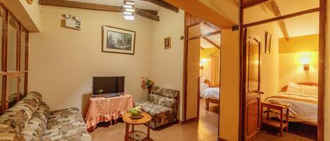 A cozy living room with a sofa, a small table with a plant, a television, and a door leading to a bedroom.