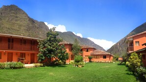 A building with a balcony, surrounded by a well-maintained lawn and a mountain in the background. -  Hotel Lilium Valley Ollantaytambo (Ollantaytambo)