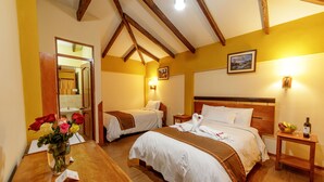 A hotel room with two beds, wooden beams on the ceiling, a wooden table with a vase of flowers, and a small table with a bottle and fruit. -  Hotel Lilium Valley Ollantaytambo (Ollantaytambo)
