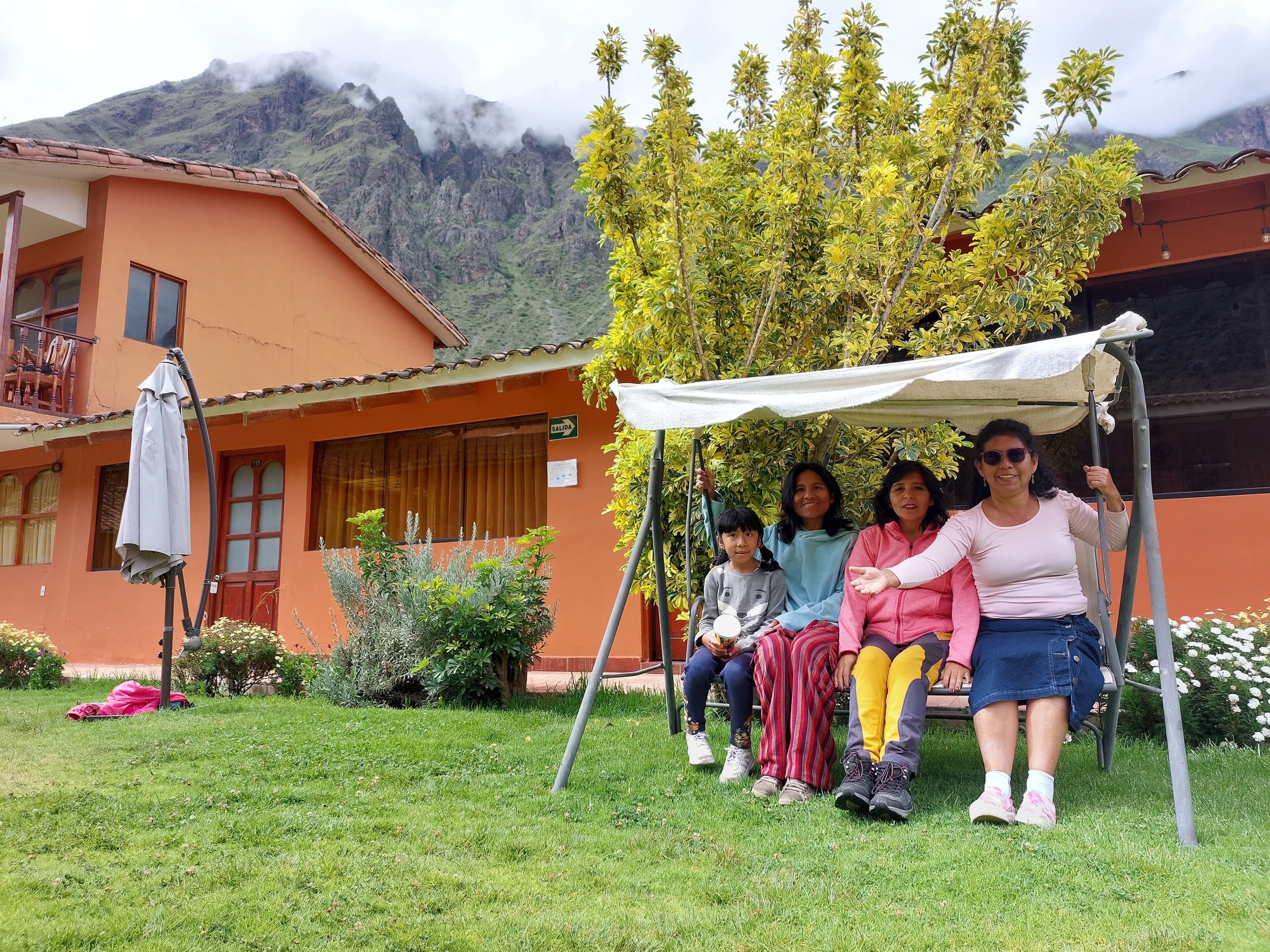 A group of people sitting on a swing in a courtyard with a mountain backdrop.