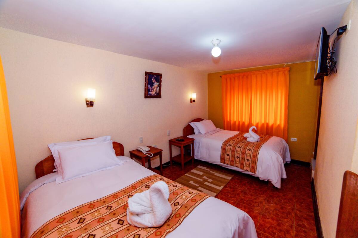 Une chambre d’hôtel avec deux lits, une petite table, un téléphone et un téléviseur fixé au mur.