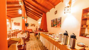 A dining area with long tables, wooden chairs, and a buffet setup with food and drink containers. -  Hotel Lilium Valley Ollantaytambo (Ollantaytambo)