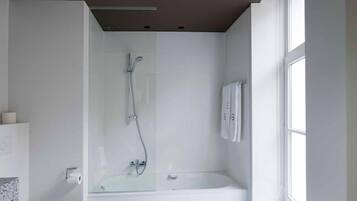Een moderne badkamer met een douchecabine van glas, een wit toilet en een groot raam voor natuurlijk licht.