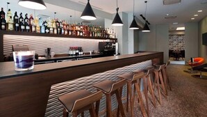 A bar area with a long counter, multiple stools, and a variety of bottles on the shelves. - Square Hotel (Kortrijk)