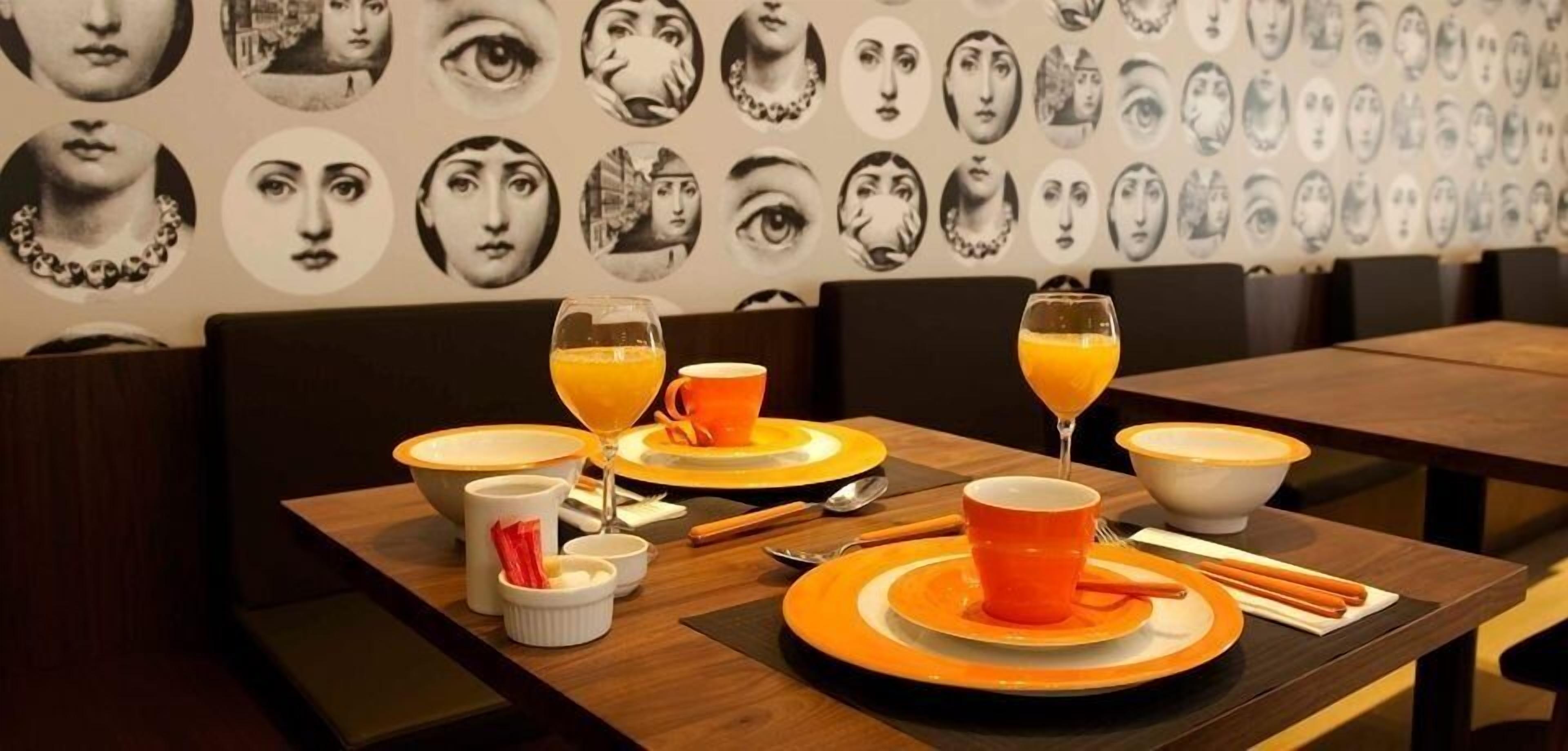 A dining table set with orange and white plates, bowls, and glasses, with chopsticks and a small bowl of condiments.