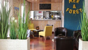 A modern interior with wooden flooring, a bar area, and seating arrangements including a yellow chair and a black leather sofa. - Hotel Mer et Forêt (Saint-Trojan-les-Bains)