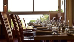 A dining area with wooden chairs and tables set for a meal, large windows with a view of greenery and a bridge. - Hotel Mer et Forêt (Saint-Trojan-les-Bains)