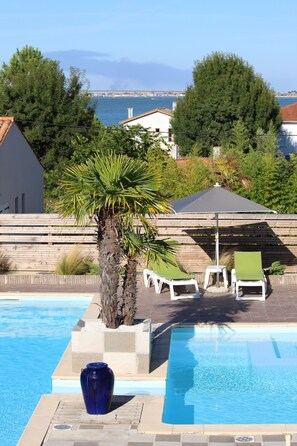 En swimmingpool med liggestole og en palme, omgivet af et træhegn og grønt.