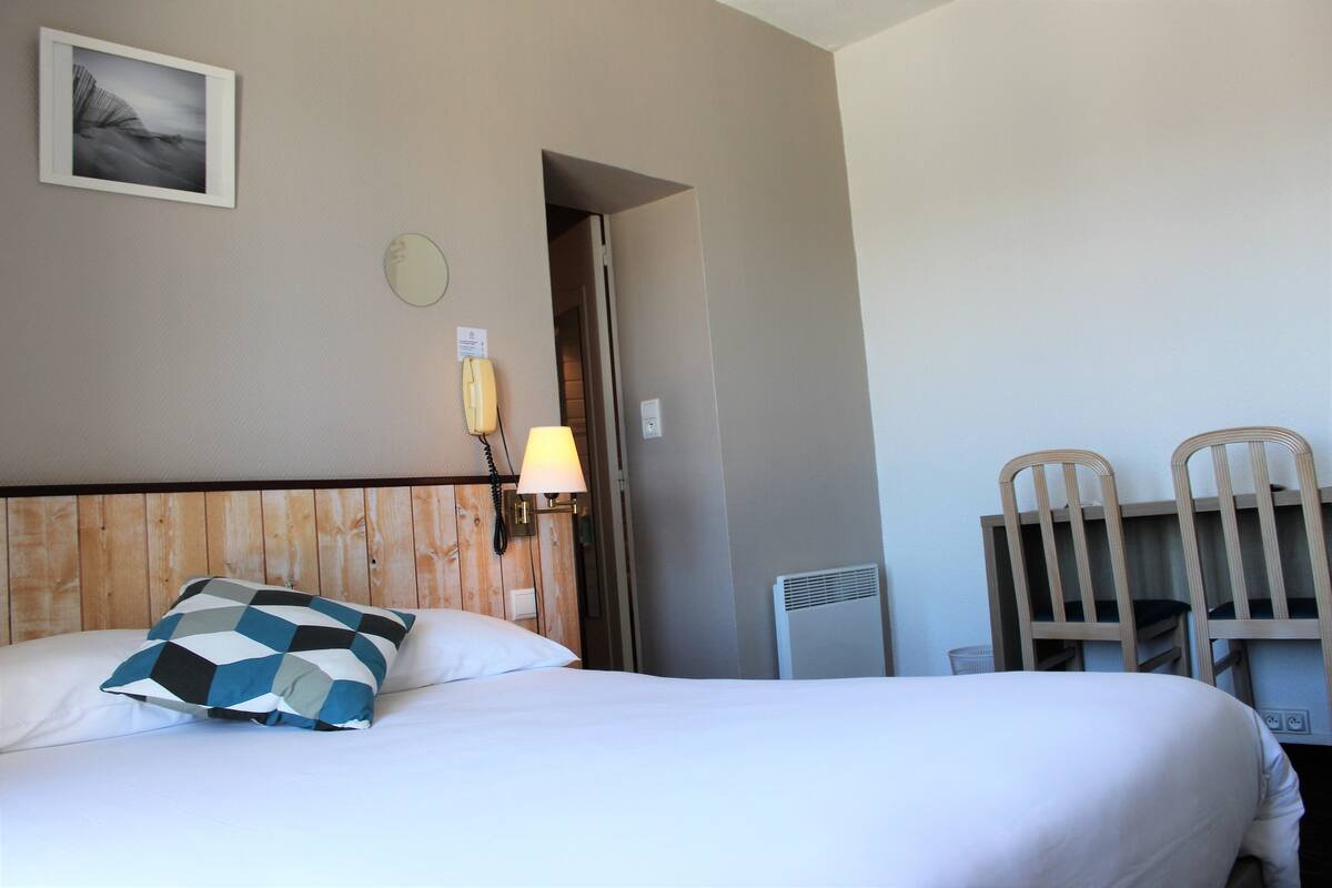 Ein Hotelzimmer mit Bett, Nachttisch mit Lampe, fest an der Wand montiertem Telefon und einer Tür zu einem anderen Raum.