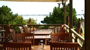 An outdoor dining area with wooden tables and chairs, overlooking a body of water and a bridge. - Hotel Mer et Forêt (Saint-Trojan-les-Bains)