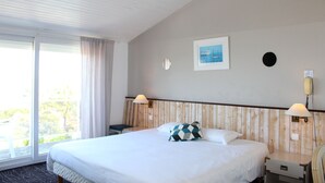 A hotel room with a large bed, a window with curtains, a wall-mounted phone, and a framed picture. - Hotel Mer et Forêt (Saint-Trojan-les-Bains)