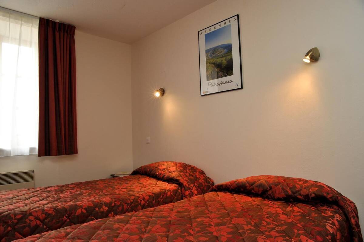 Une chambre avec deux lits, une fenêtre avec des rideaux, une affiche au mur et deux lampes fixées au mur.