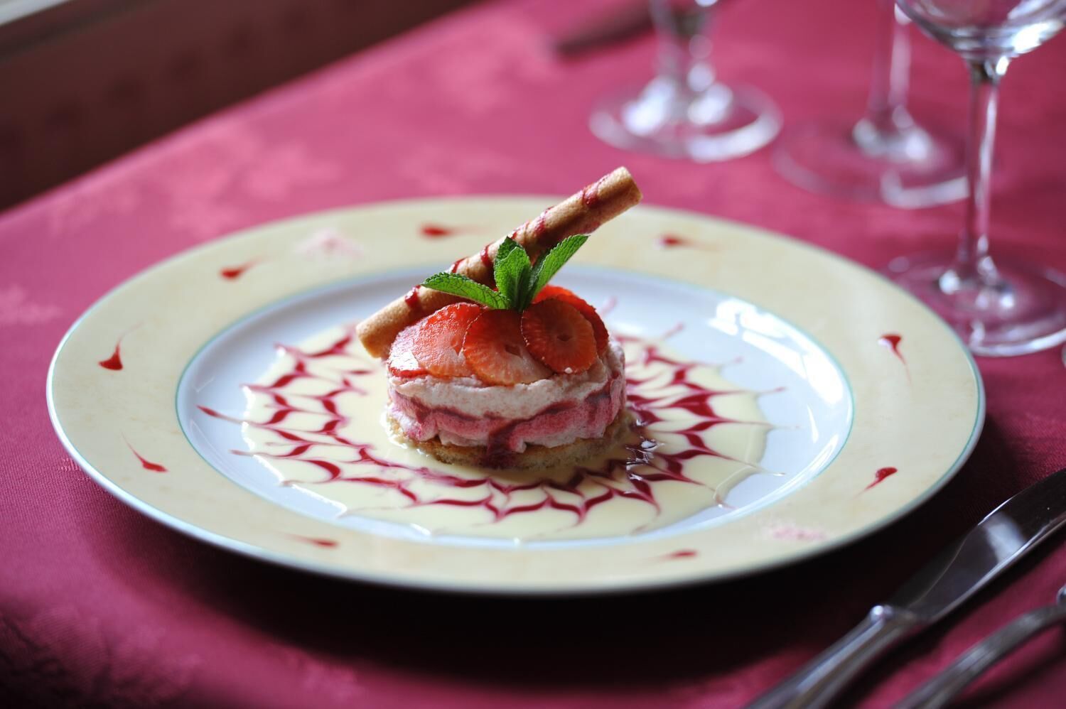 A dessert on a plate with a decorative pattern, accompanied by a fork and knife on a tablecloth.